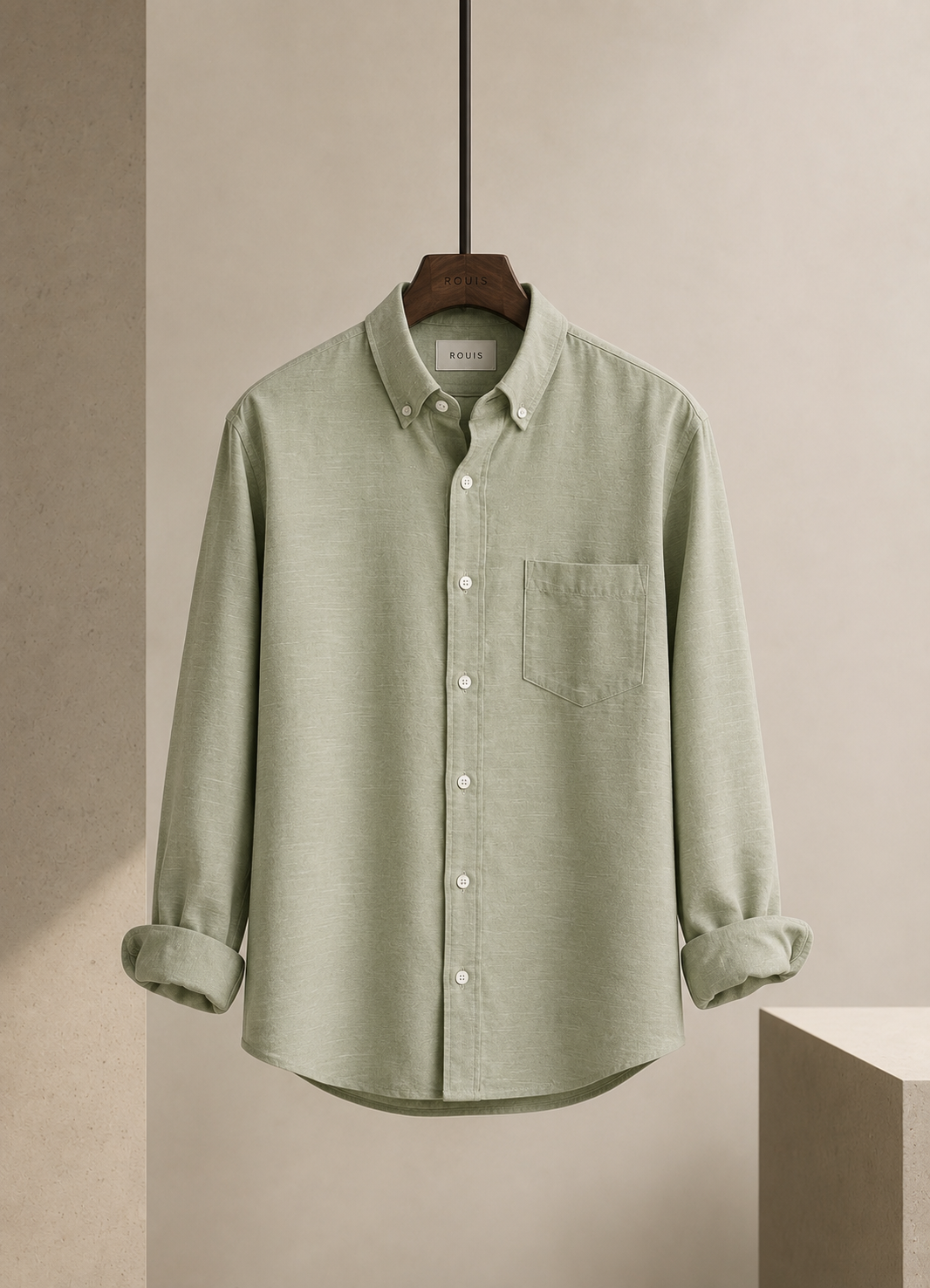 A light sage green long-sleeve button-down shirt by Brunello Cucinelli, hanging on a wooden hanger against a neutral beige background.